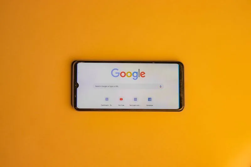 Móvil con la página de inicio de Google abierta, sobre un fondo amarillo