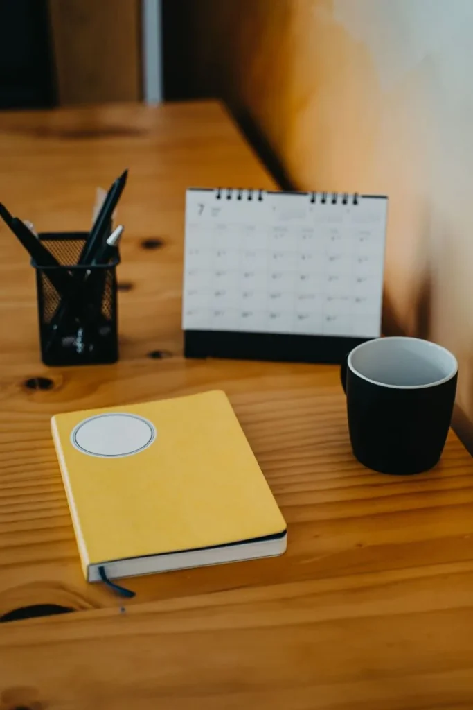Calendario de mesa, libreta amarilla, taza y lapicero sobre un escritorio de madera, listos para organizar la semana